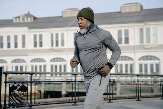 Concentrated African American bearded aged male athlete with closed eyes in activewear running on city street in sunny day