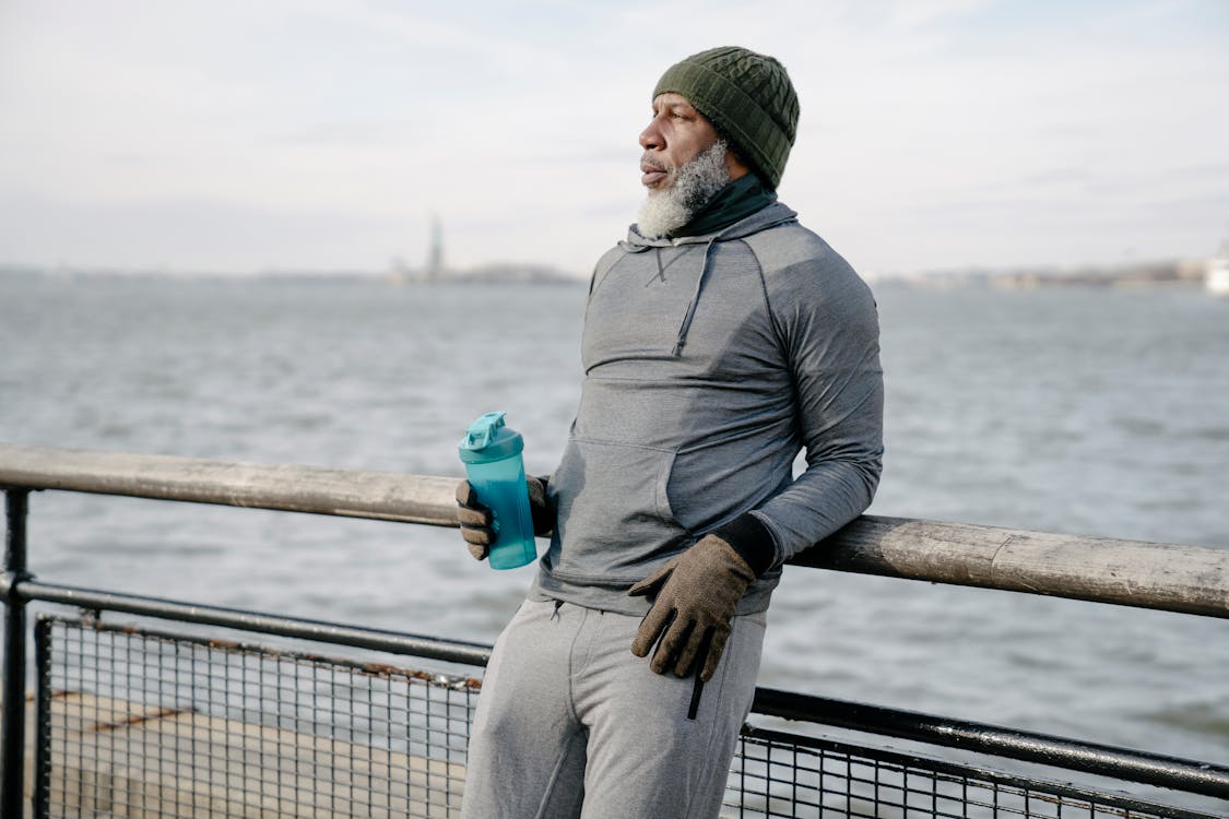 Black elderly man in sportswear standing on embankment near sea