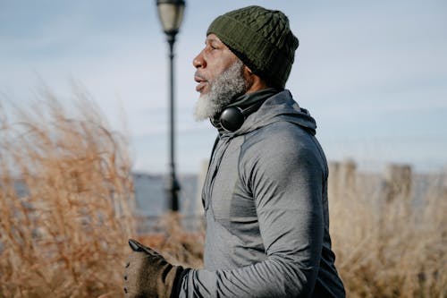 Side view of concentrated senior African American male in warm activewear running in park near sea and looking away thoughtfully in daylight