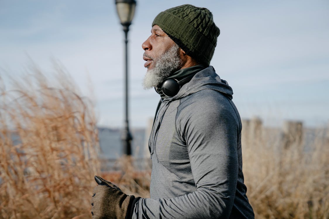 Side view of concentrated senior African American male in warm activewear running in park near sea and looking away thoughtfully in daylight