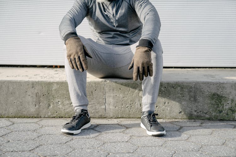 Crop Faceless Man In Gray Outfit Sitting On Curb