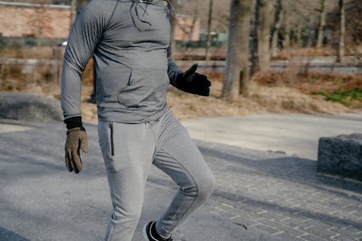 A man in activewear jogging outdoors during the day, showcasing fitness and health.