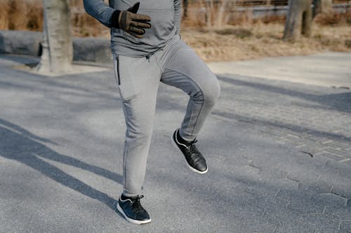 Free Crop anonymous male in gray sport trousers and black sneakers warming up legs in asphalt road Stock Photo
