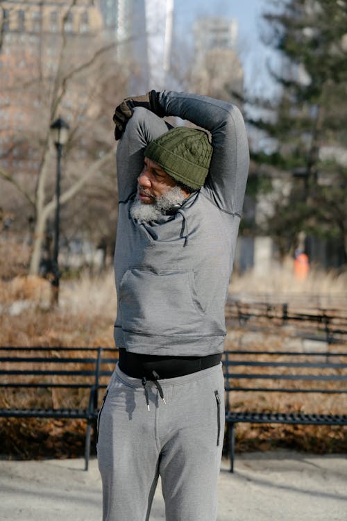 Elderly African American male athlete in sportswear stretching triceps of raised arms while doing exercises in park