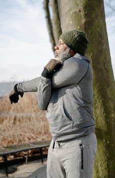 Side view of mature concentrated black male in warm sportswear stretching arms in park