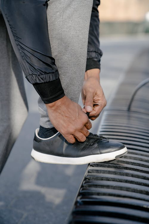 Crop black person tying lace of sneaker on street