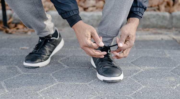 Crop Ethnic Man Tying Shoelace On Pavement