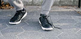 Crop unrecognizable person in sneakers with untied shoelace walking on cobblestone pavement in daytime
