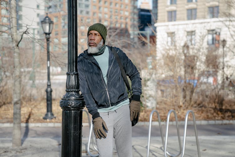 Black Senior Man Leaning On Post In Autumn Street