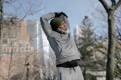 Black elderly male stretching arms in park in autumn