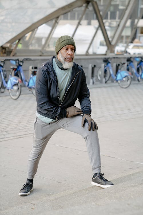 Free Full body of aged gray haired African American male athlete wearing warm sportswear warming up on staircase in city park and looking away Stock Photo