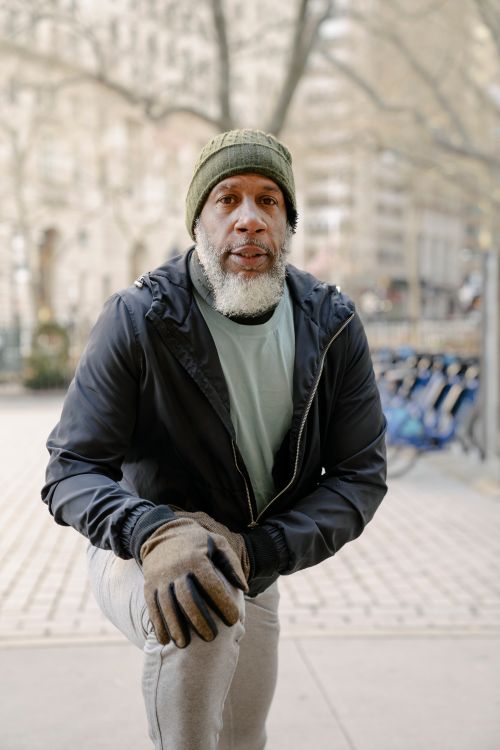 Free Senior bearded African American male in windbreaker jacket and sport trousers warming up legs in park Stock Photo