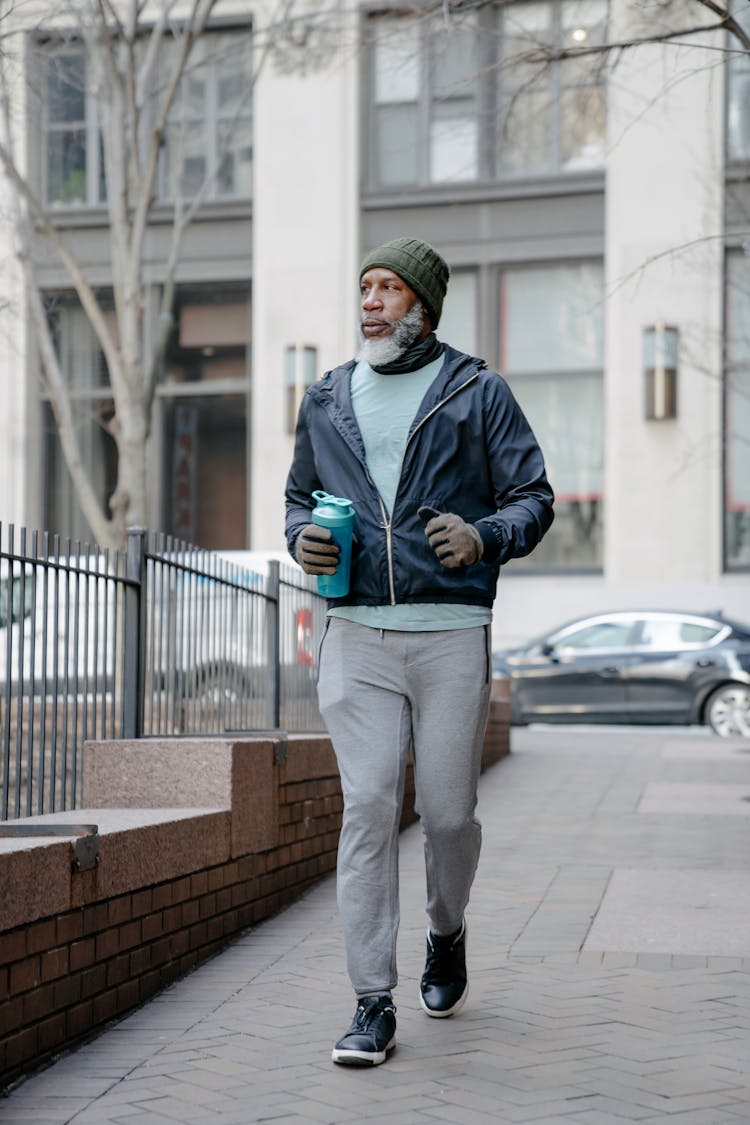 Black Senior Man In Activewear Strolling Along Fence On Pavement