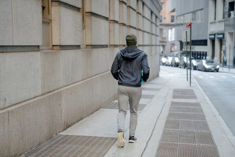 Man In Casual Activewear Jogging On Paved Sidewalk In City