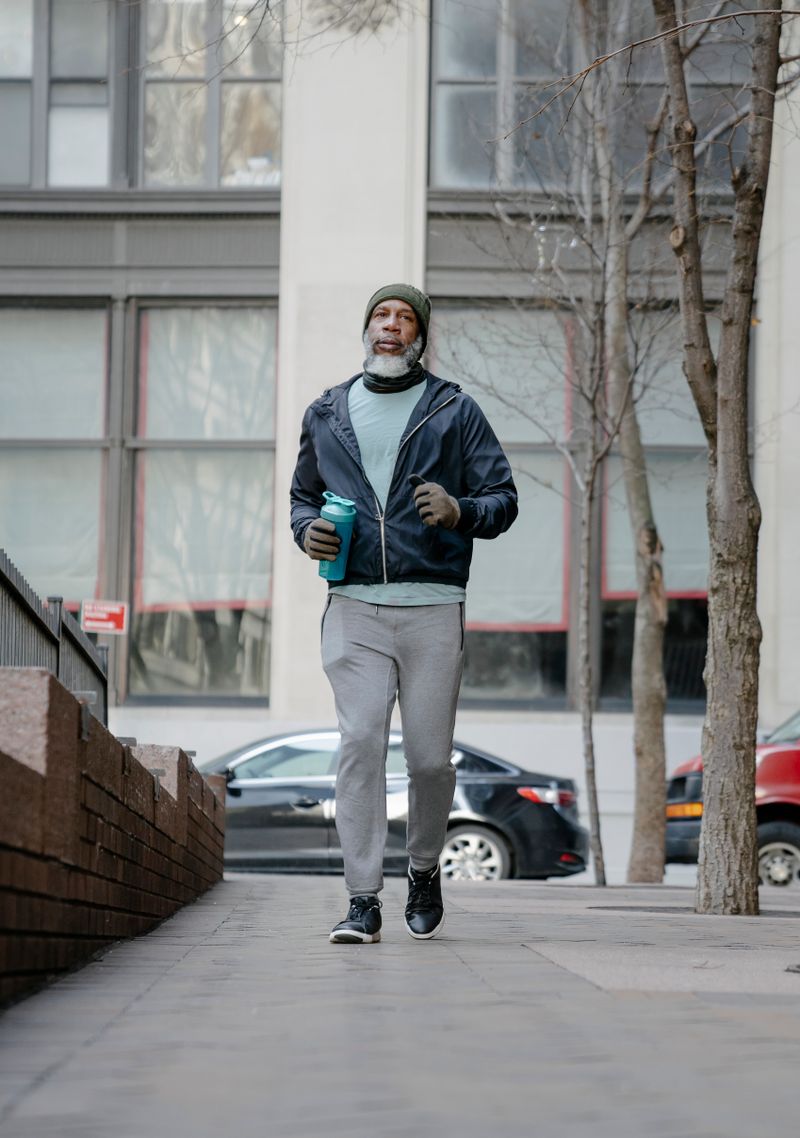 An older adult jogging along a city sidewalk.