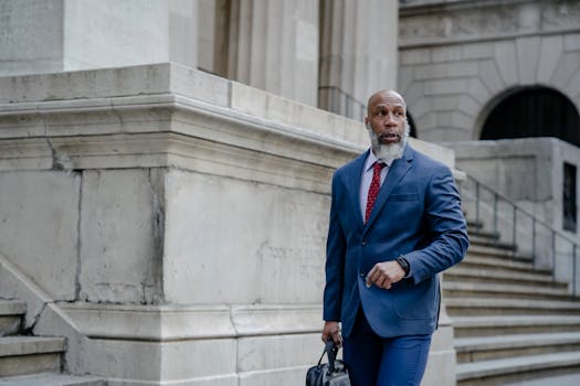 Concentrated African American mature entrepreneur in formal blue suit with leather handbag walking along entrance of building