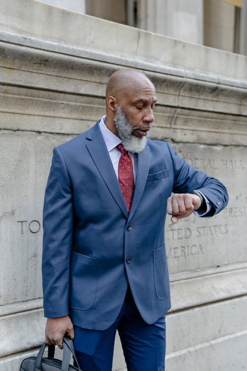 Confident bearded black man in classy suit checking time on wristwatch