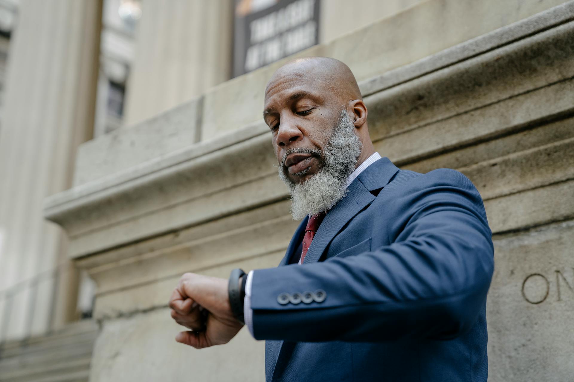 African American man in a suit checking time on a watch outside an office building.