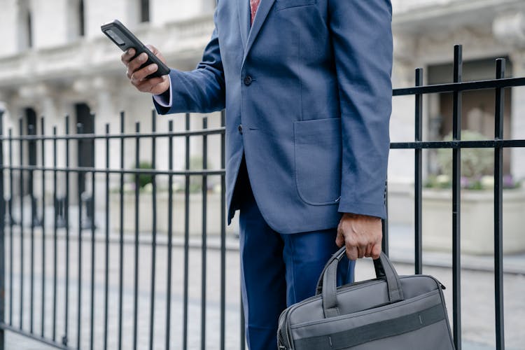 A Person In A Suit Using A Cellphone While Holding A Briefcase