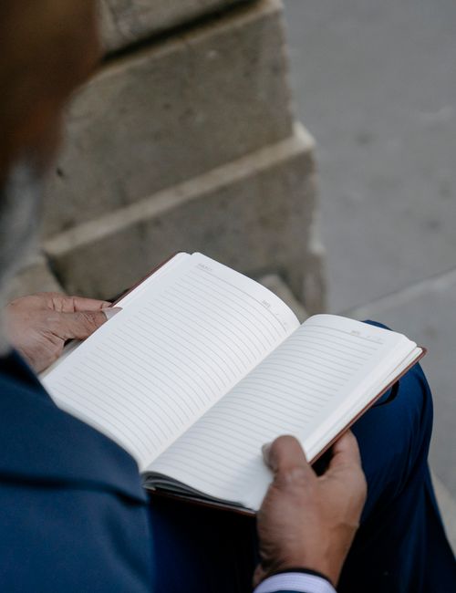 Close-up of a person holding an open notebook while seated outdoors, showing blank pages.