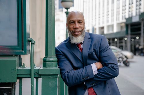 Free Smiling businessman in blue suit leaning against a railing in a city street. Stock Photo