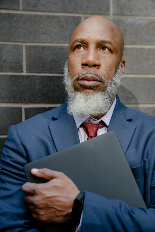 Free A Man in a Suit Holding a Laptop Stock Photo