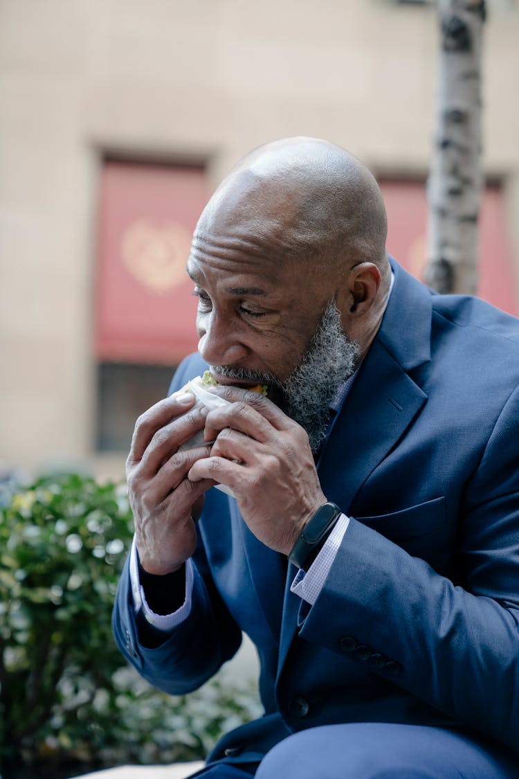 Man In Blue Suit Eating A Sandwich