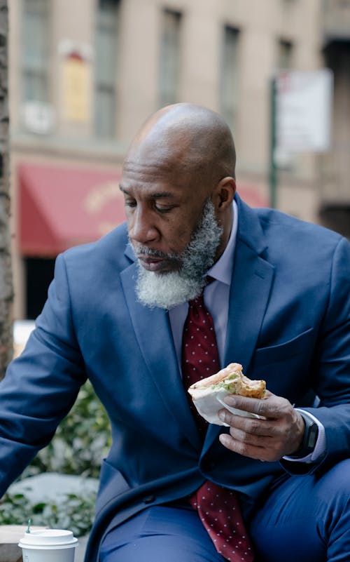 Man in Blue Suit Jacket Eating Burger