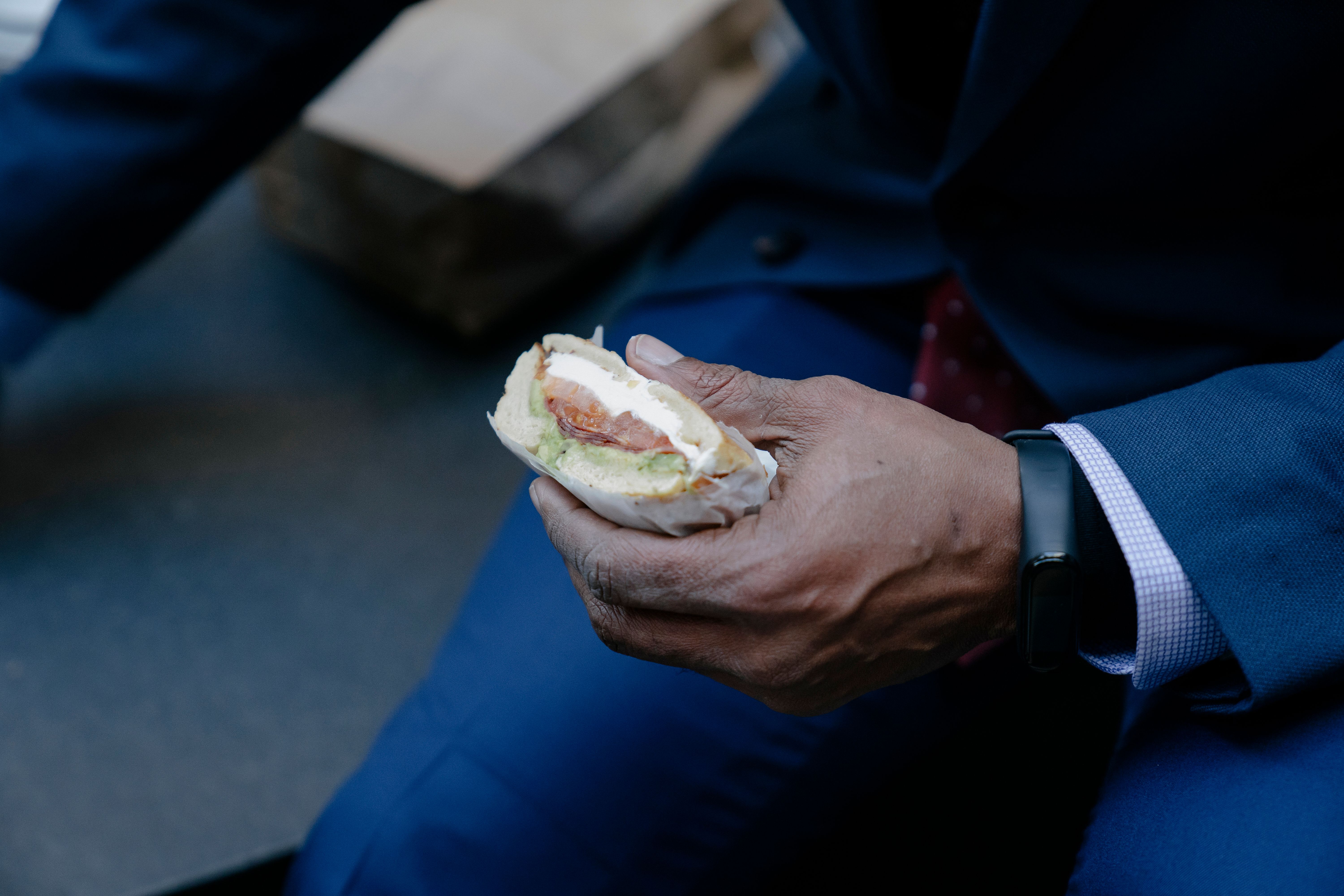 A businessman in a suit enjoys a sandwich during a break, showcasing a lifestyle moment.