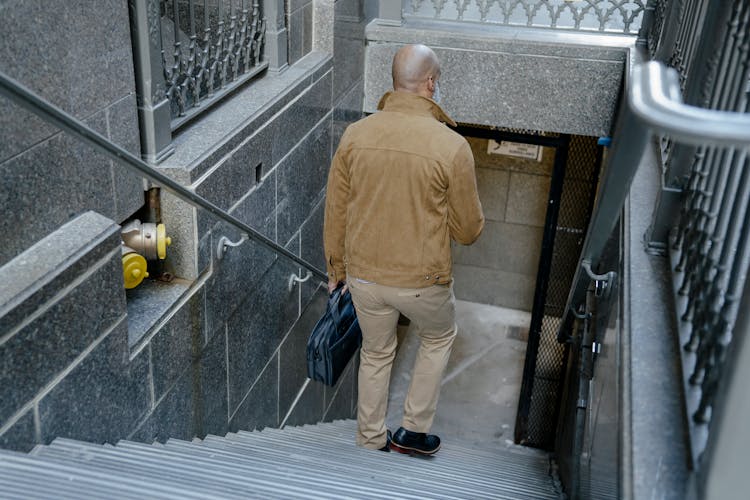 Back View Of A Man Walking Down Stairs While Holding A Briefcase