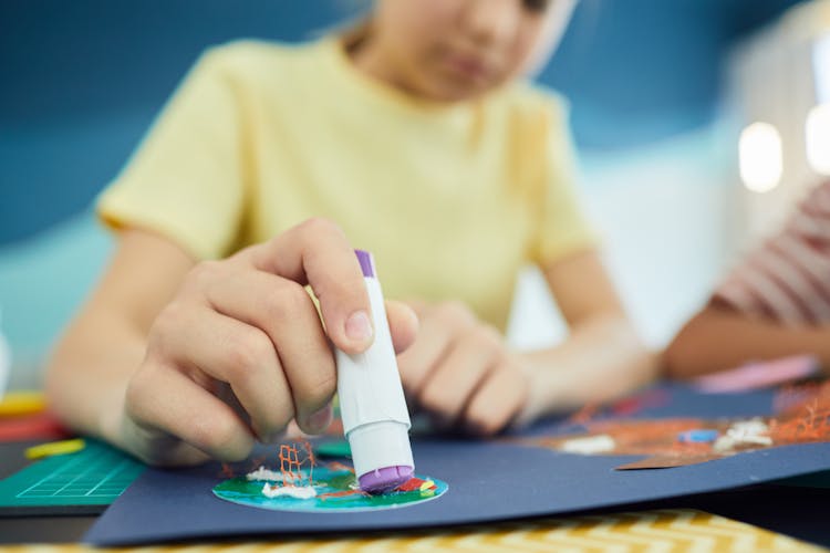 Girl Hand Holding Glue Over Paper