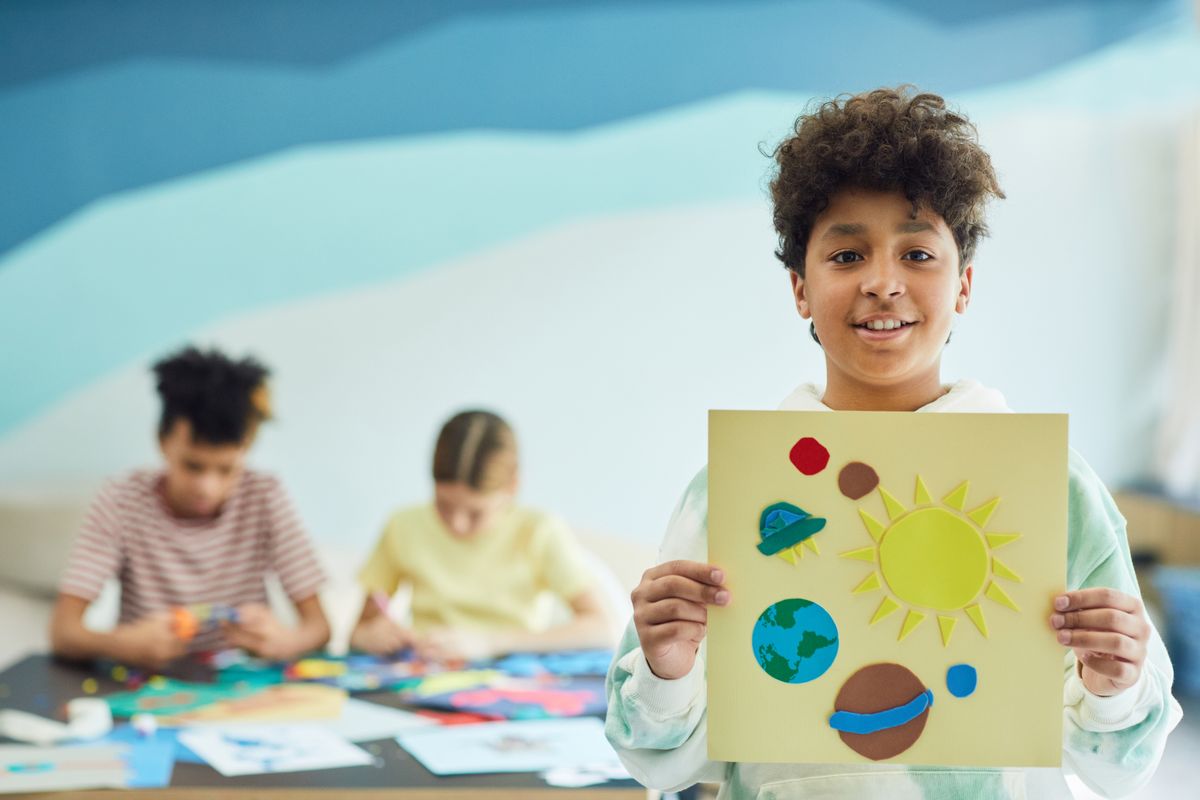Smiling child holding up a colorful solar system art project in a classroom