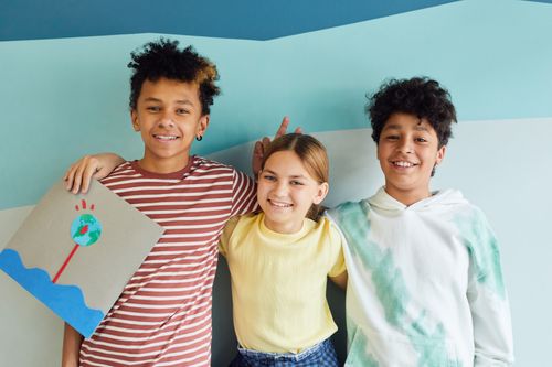 Free Three happy children smiling and posing with a creative artwork in a colorful indoor setting. Stock Photo