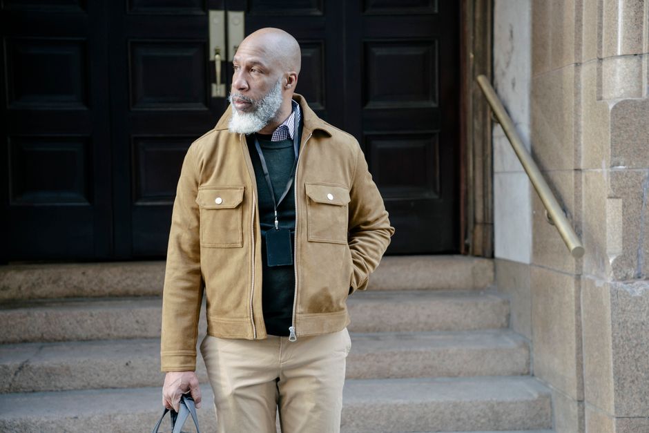Man with beard wearing a stylish brown jacket poses outdoors by stairs in an urban setting. Man with beard wearing a stylish brown jacket poses outdoors by stairs in an urban setting.