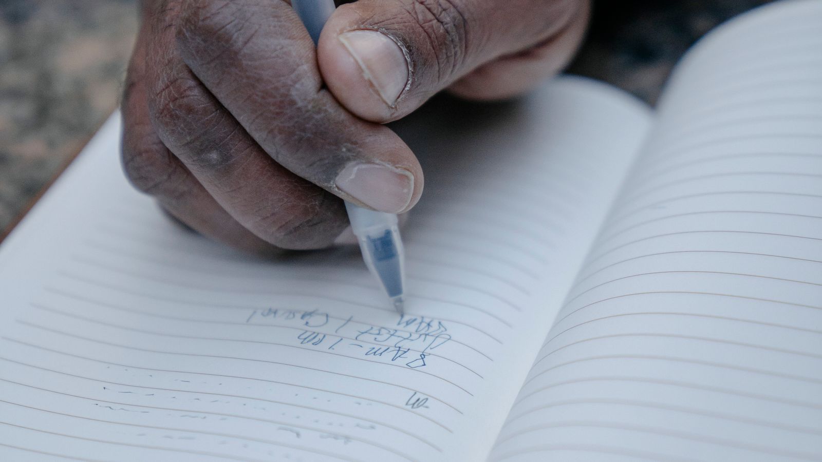 A hand writing with a clear-barrel pen in a lined notebook