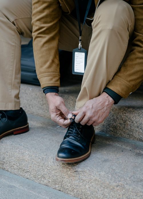 Free Close-up of a man tying shoelaces on black dress shoes, sitting on stone steps in a business attire. Stock Photo