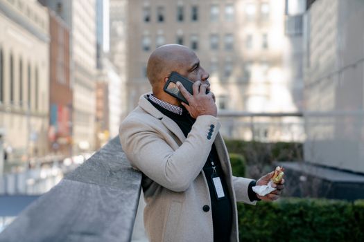 Man in White Jacket Talking on the Phone with a Sandwich in Hand 