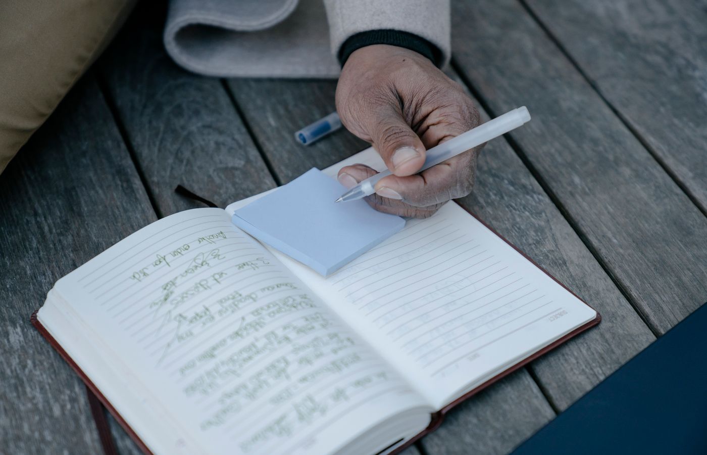 Person writing in a journal, focusing on hand holding pen with notepad on a wooden table.