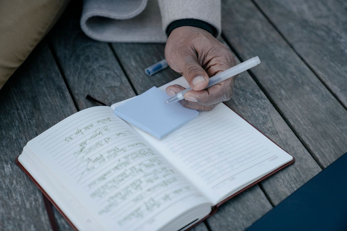 A person writing notes in an open journal on a wooden table.
