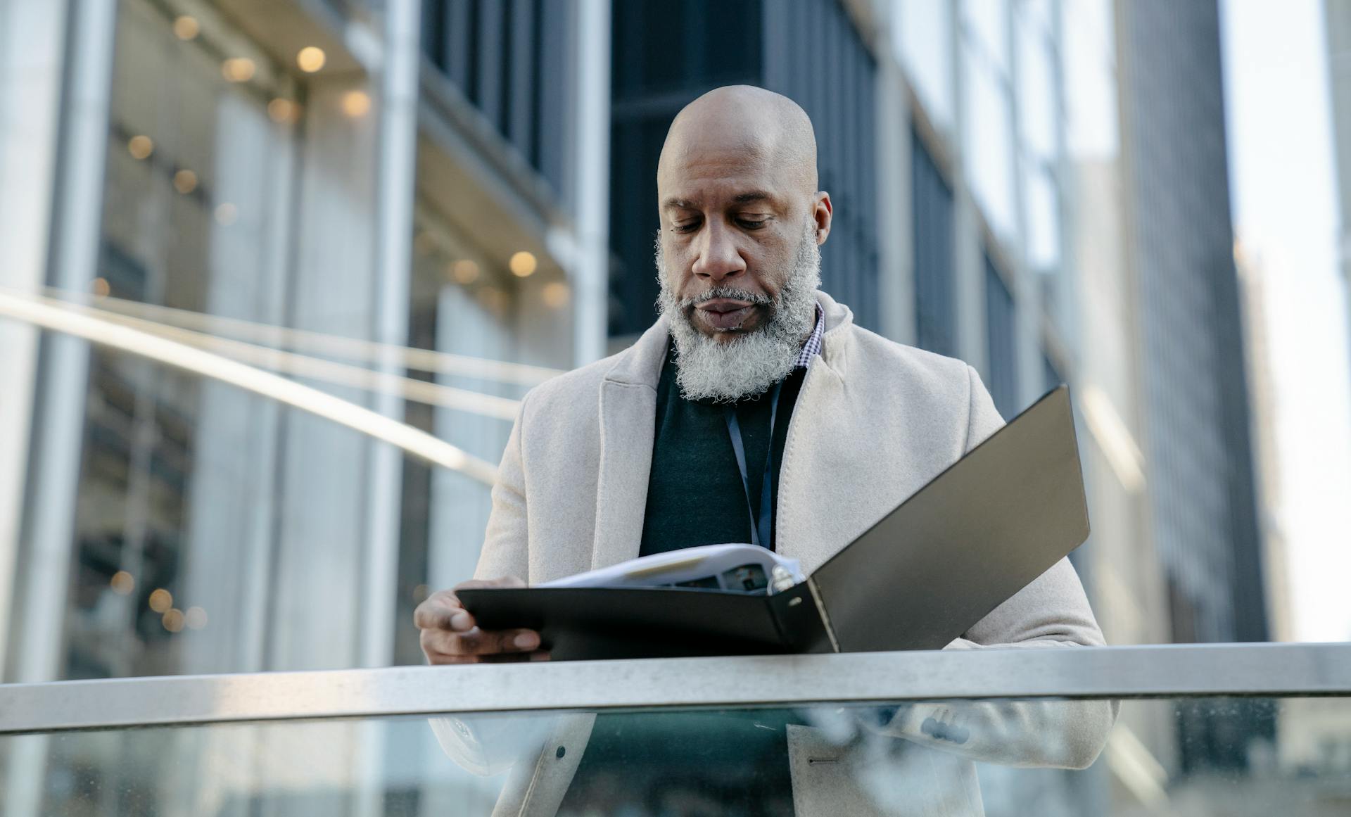 African American man reading a book outside modern office buildings in a city setting.