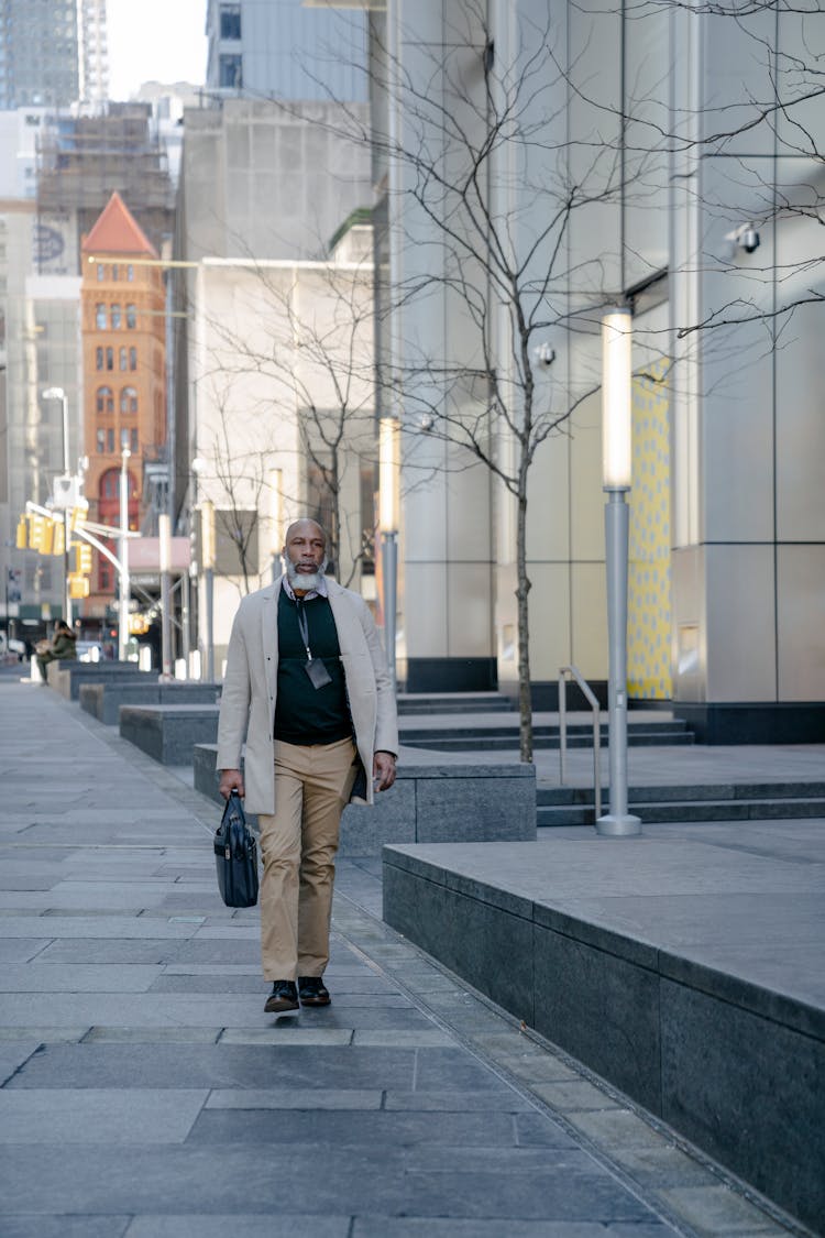 A Bald Man Walking While Carrying Handbag