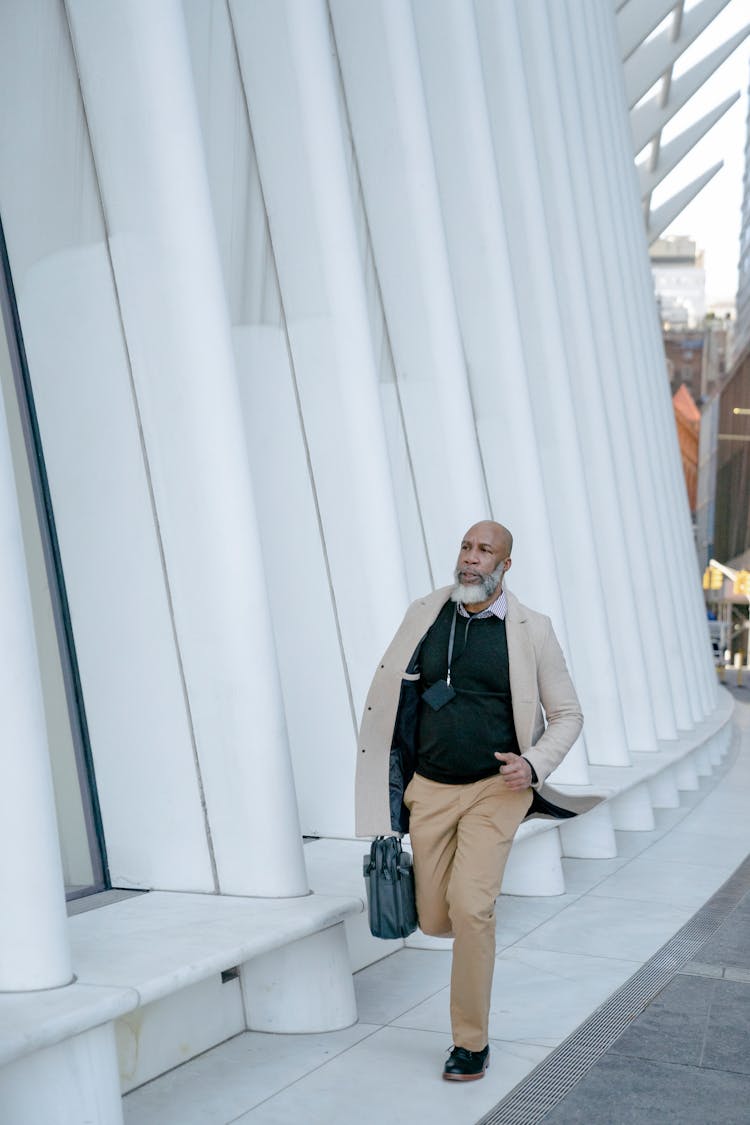 Man Wearing A Coat Walking With A Briefcase By A Modern Building