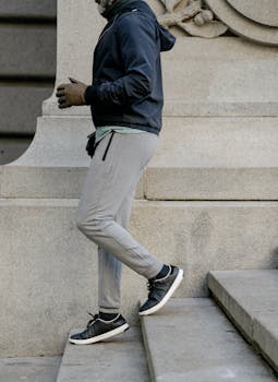 A man wearing sports clothing walks on stone steps in an urban setting, focusing on fitness and active lifestyle.