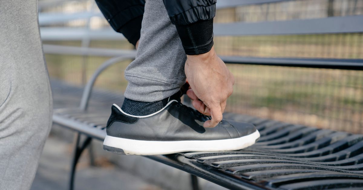 Close-up of a person tying sneakers on an outdoor park bench, preparing for exercise.