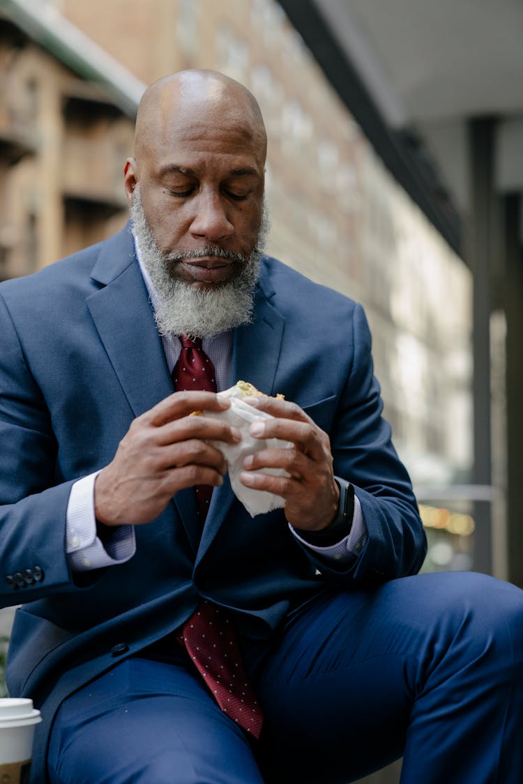 Man In Blue Suit Eating A Sandwich