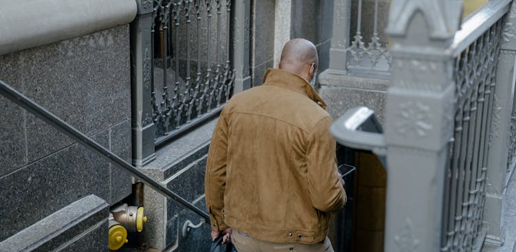 Back View Of A Man Walking Down The Stairs In City Holding His Phone 