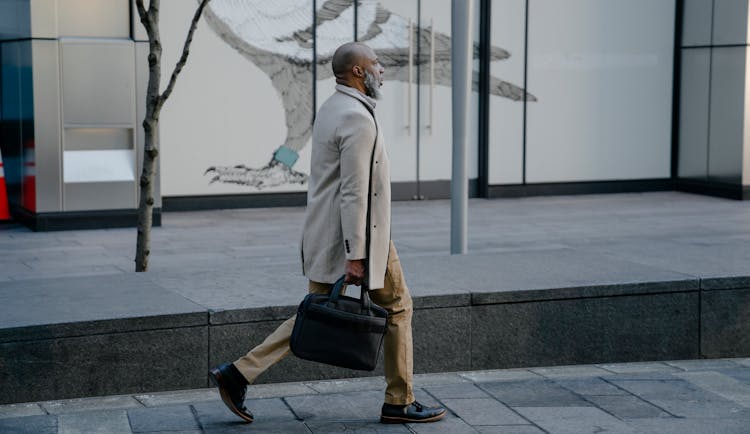 Mature Man With A Gray Beard Walking In City Holding A Laptop Bag 