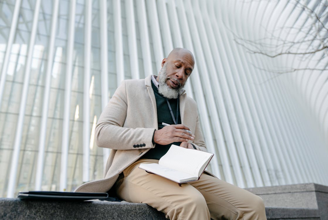 Man in Beige Blazer Sitting on Chair Reading Book