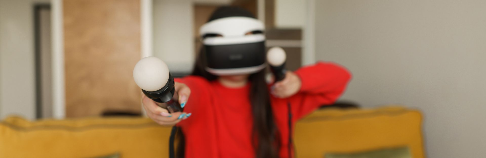 Adult woman wearing VR headset and using controllers in a living room.