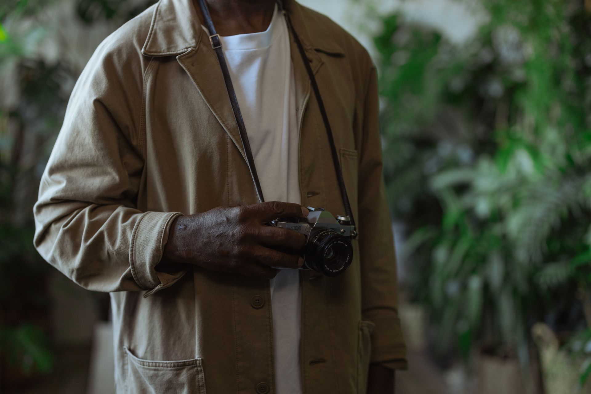 A person holding a vintage camera indoors surrounded by greenery, showcasing analog photography charm.